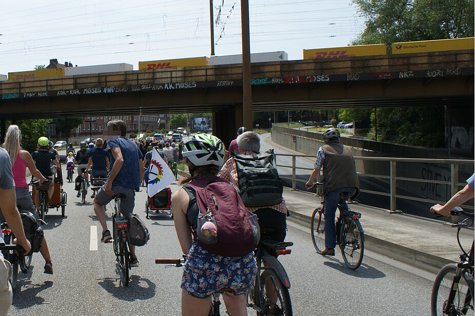 Alle wichtigen Verkehrsmittel auf einem Bild Die Fahrraddemo fährt unter einer Eisenbahnbrücke hindurch, auf der ein Güterzug steht.